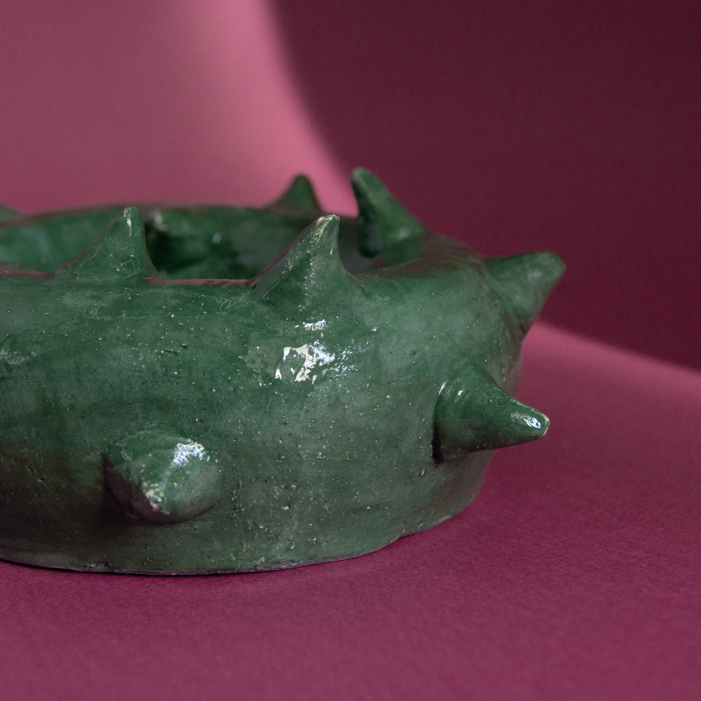 Green thorn-inspired ashtray with spikes, measuring 18 cm in diameter, set against a pink background.
