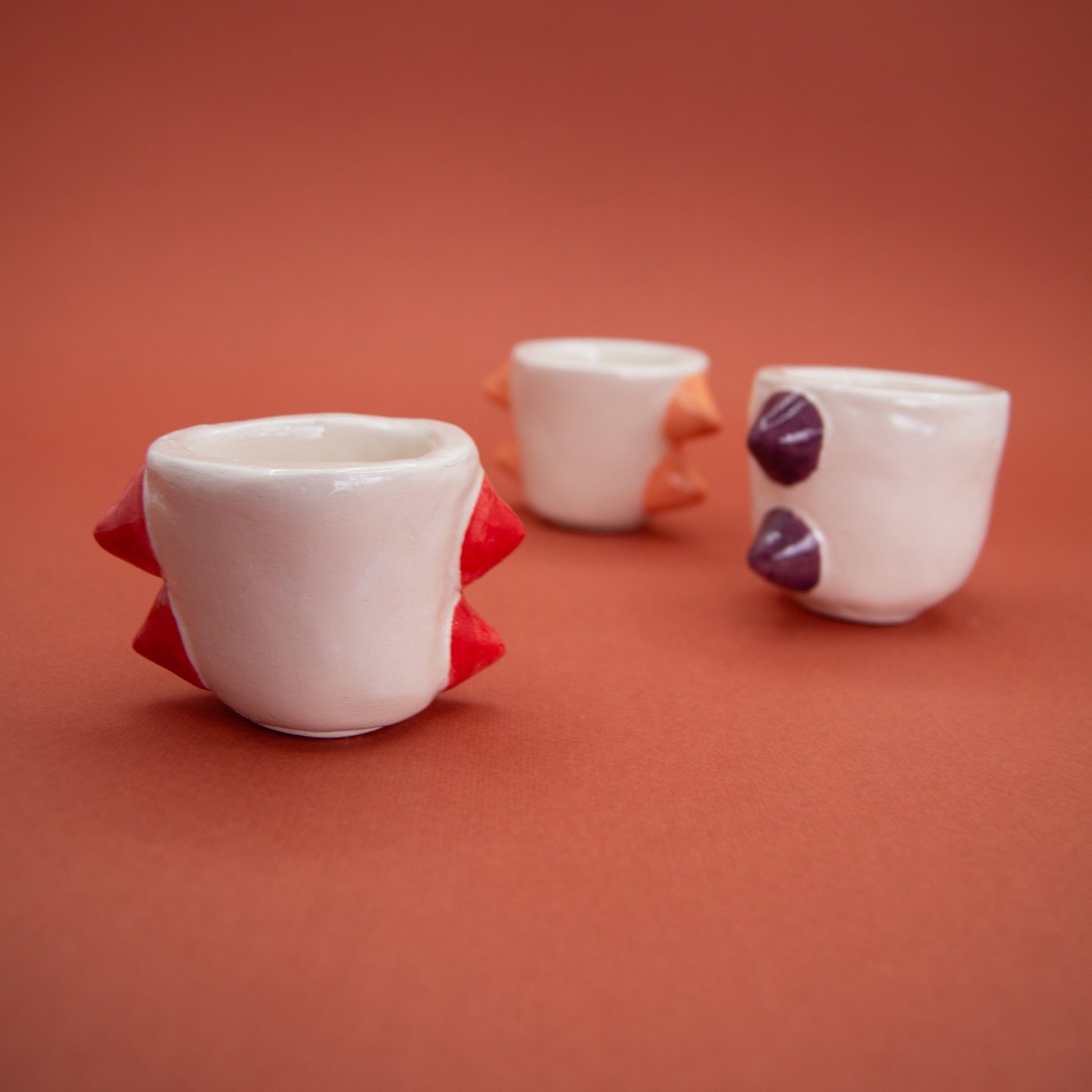 Set of three espresso coffee cups in red, purple, and pink with stud-like details and unique textures, perfect for stylish serving.