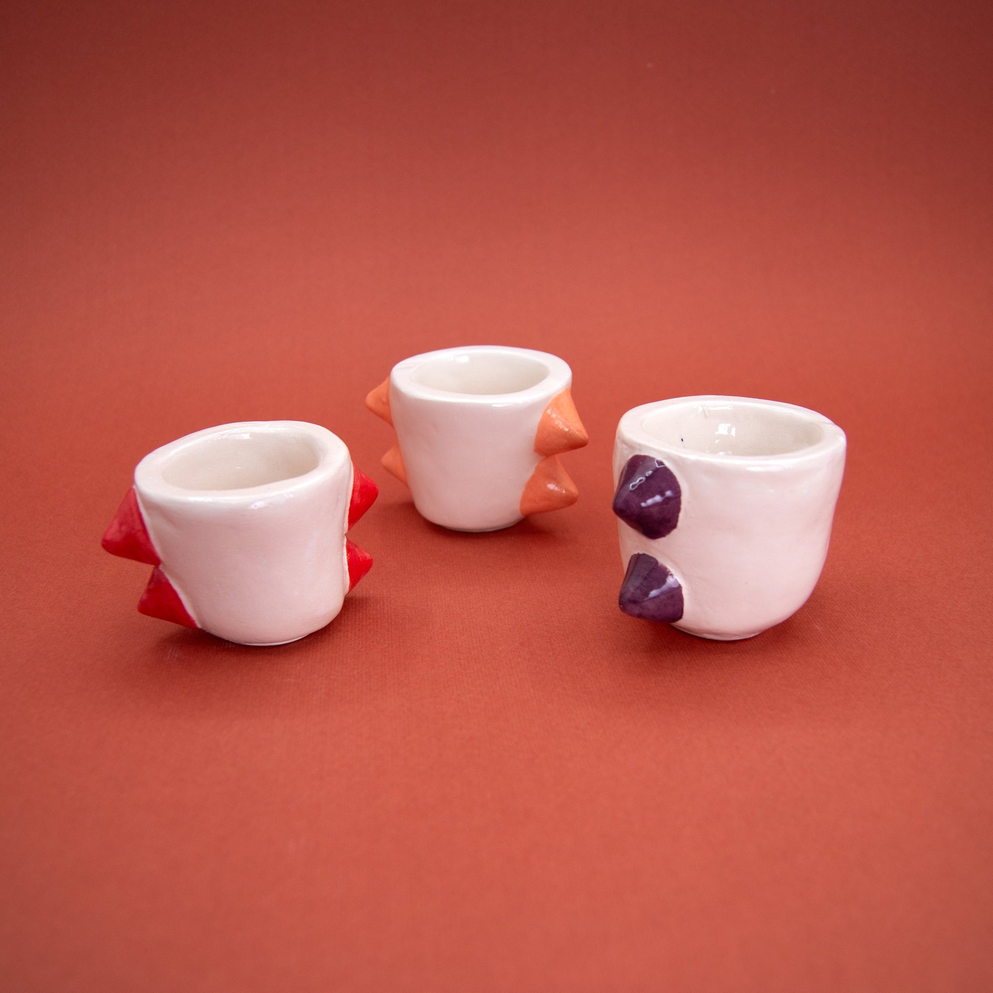 Set of three espresso cups with stud-like details in red, purple, and orange on a vibrant background.